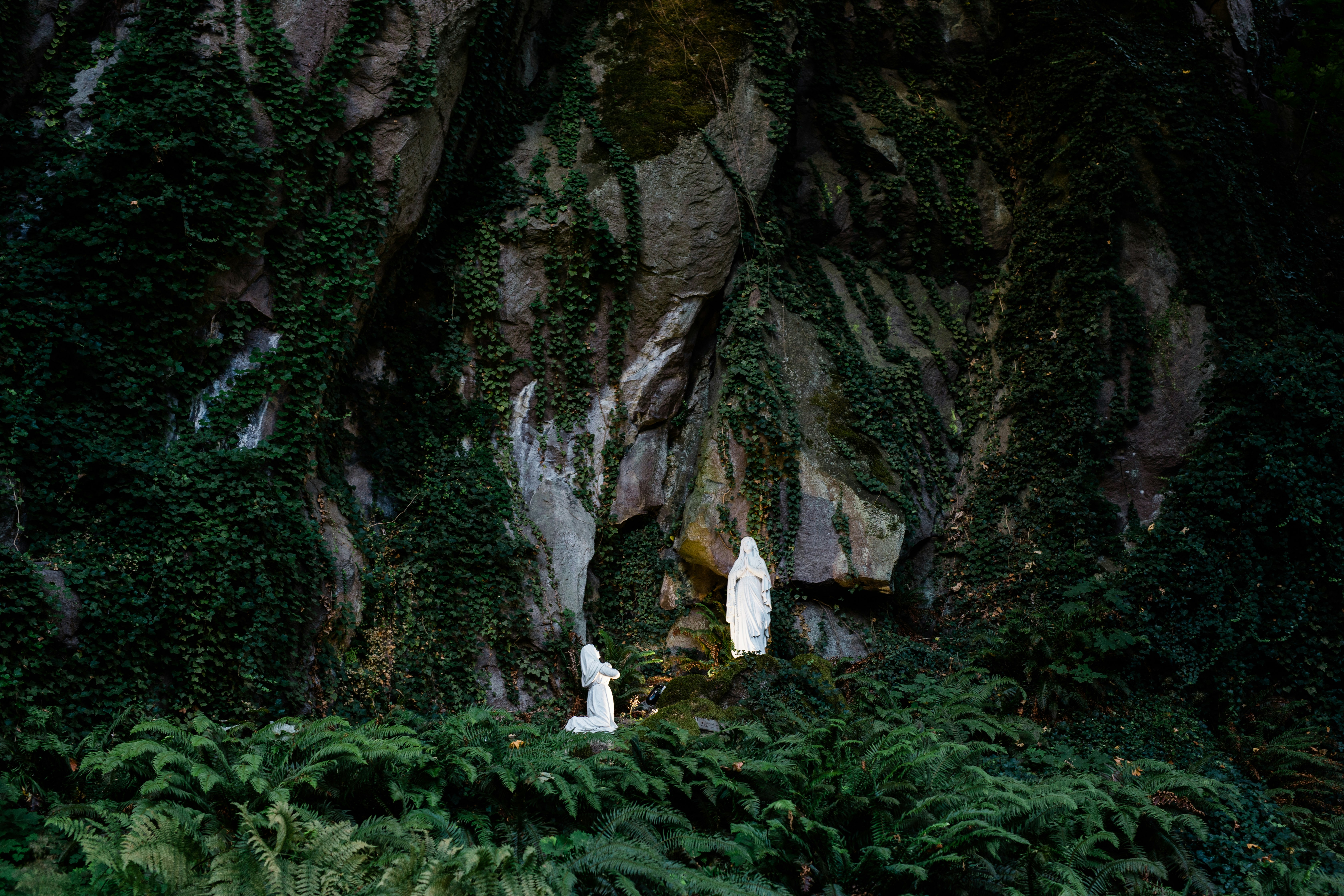 person in white shirt standing on green grass near gray rock formation during daytime